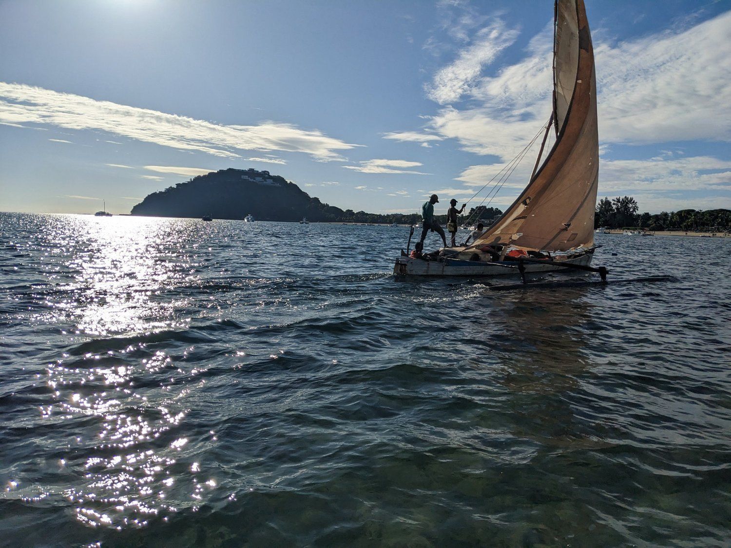 A traditional sailing boat on calm water near a hilly island at golden hour